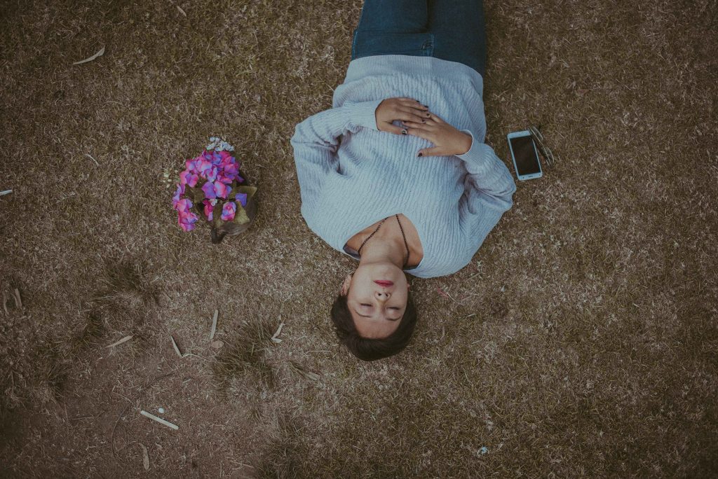 person lying on the ground next to a phone and a bouquet of pink flowers