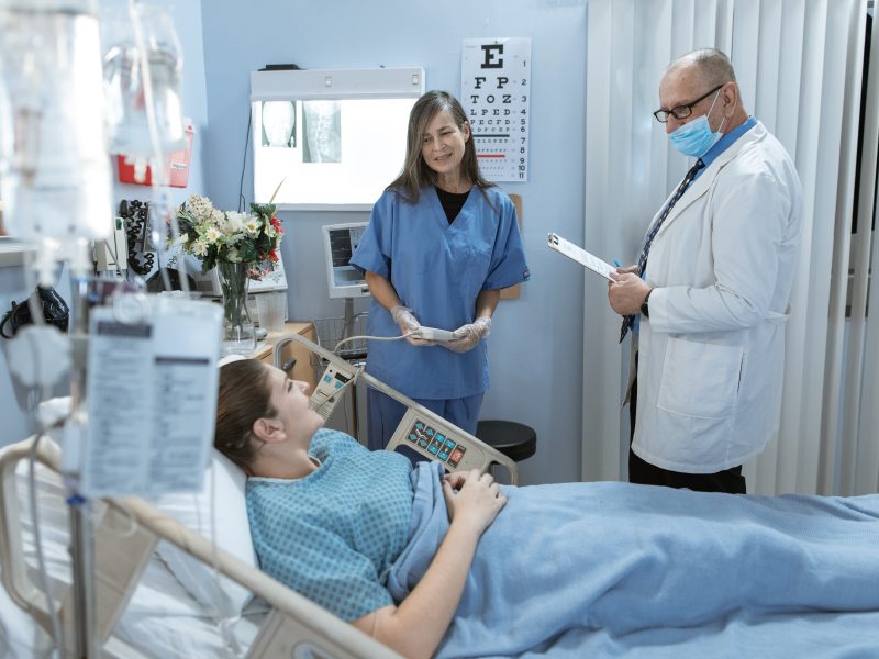 A woman who is a patient talks with a doctor and a nurse from a hospital bed.